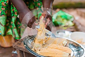 Black woman hands cutting corn from cub while cooking traditional african dish with african dress
