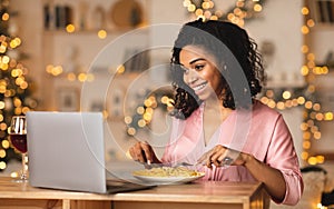 Black woman having dinner during virtual date on laptop