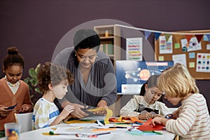 Black woman helping group of little children doing crafts in preschool class