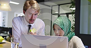 Black woman with hijab meeting business man in casual startup office, man eating apple on meeting