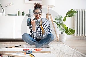 Black woman holding electric drill tool to assembly furniture in new home