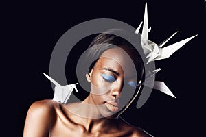 Black woman, makeup and fine art with beauty, cosmetics or origami birds on a dark studio background. Closeup or face of