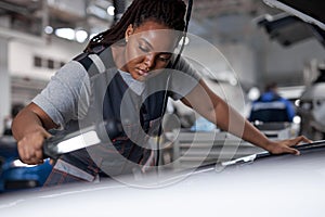 black woman mechanic looking to car engine and holding lamp, Car master in service shop