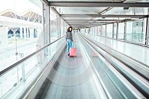 Black woman in the moving walkway at the airport with a pink sui