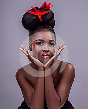 Black woman, portrait and origami bird in studio isolated on gray background with makeup for aesthetic. Cosmetics, smile