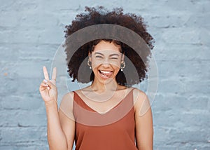 Black woman, portrait and tongue out with peace sign and afro against a gray wall background. Happy and goofy African