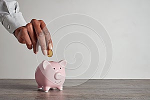 Black woman putting coin in piggy bank to save money