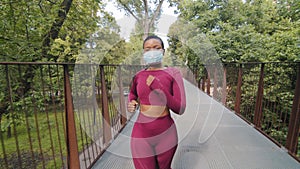 Black woman running on bridge in protective medical mask. Young plus size athletic beautiful female in activewear