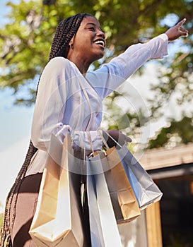 Black woman, shopping bags and outdoor on city street while happy and hailing for a taxi or cab to travel on consumer