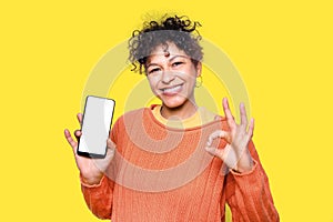 Black woman showing and pointing at blank screen smartphone on yellow background