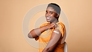 Black Woman Showing Vaccinated Arm After Vaccine Injection, Beige Background