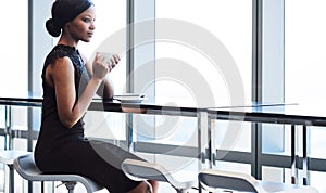 Black woman sitting on bar chair next to large window