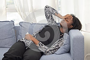 Black woman sitting on the couch whiles Sneezing with tissue