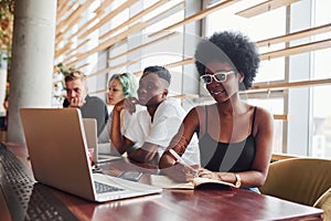 Black woman sitting in front of group of multi ethnic people with alternative girl with green hair is working together