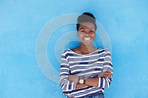Black woman smiling with arms crossed against blue background