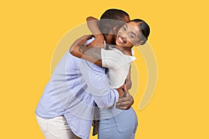 Black woman smiling over shoulder while hugging man on yellow background