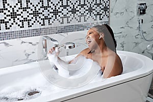 Black woman taking bath with bubbles in bathroom interior, singing in shower handle, have fun