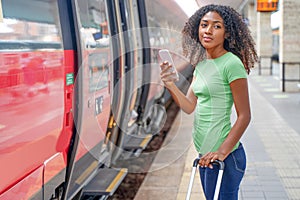 Black woman taking the train in station platform holding phone