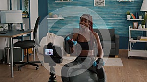 Black woman trainer practicing morning yoga exercise sitting on fitness swiss ball