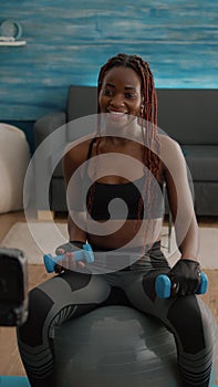 Black woman trainer practicing morning yoga exercise sitting on fitness swiss ball