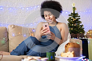 Black Woman using smart phone on Christmas eve. Black woman celebrating holiday festivities at home