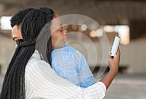 Black woman using smartphone while hugging with her boyfriend outdoors