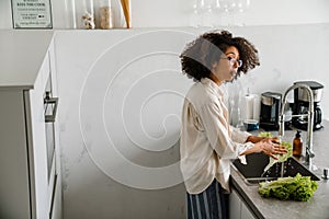 Black woman washing lettuce while cooking at home