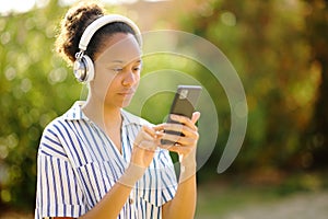 Black woman wearing headphone using phone in a garden
