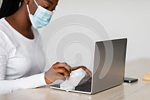 Black woman wearing medical mask cleaning laptop keyboard