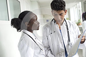 Black woman and white male doctors. A pair of young doctors of mixed race in white coats with a folder in their hands discussing