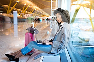 Black woman working with laptop at the airport waiting at the wi