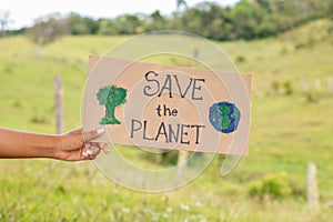 Black woman& x27;s hand holding a sign asking to save the planet on a green, natiraleza background. Care for nature and trees