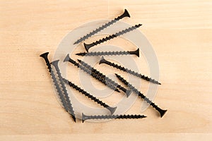 Black wood screws on wooden background.