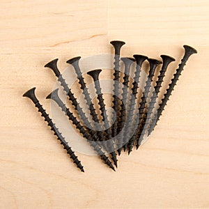 Black wood screws on wooden background.