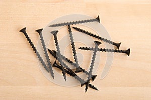 Black wood screws on wooden background.