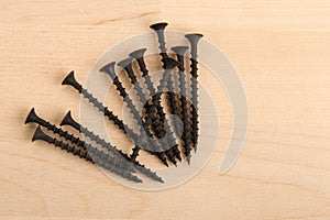 Black wood screws on wooden background.