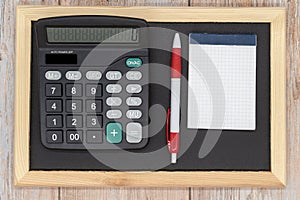 Black wooden blackboard, calculator, pen and electronic whiteboard. Top view. Copy space. Taxes, mathematics, investments, costs,