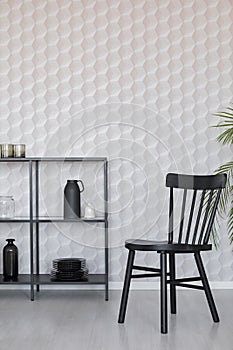 Black wooden chairs next to metal shelf with vases, plate and accessories on empty wall wall with unique wallpaper, real photo