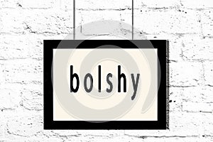 Black frame hanging on white brick wall with inscription bolshy photo