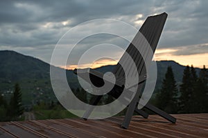 Black wooden patio chair on terrace with mountain view at sunset
