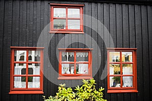 Black wooden plank wall with four Windows. Background, texture. Fragment of a traditional north-europian house wall. Four red