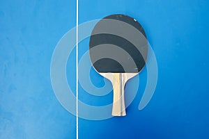 Black wooden racket for ping pong lying on the blue table top view