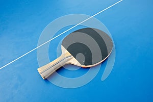 Black wooden racket for ping pong lying on the blue table top view