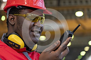 Black Worker In Protective Workwear Talking On Radio Communication Equipment In A Factory