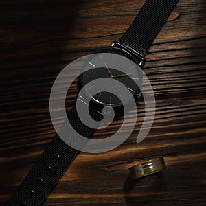 Black wrist watch and golden ring on wooden background