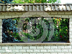 Black wrought iron fence in white concrete wall and lush green garden