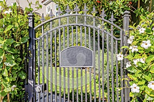 Black wrought iron gate with address number sign and doorbell on the side