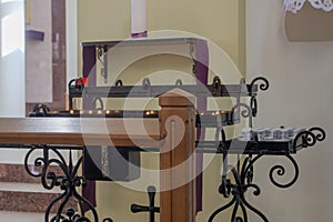 Black wrought metal pedestal for Church candles with flourishes on edges, cross and donation box in middle, prayer stand in front