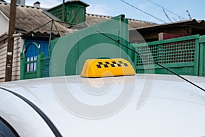 black-yellow checker taxi on a white car on a background of a green fence
