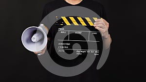 Black and yellow Clapper board or movie slate and Megaphone in man hand isolated on black background
